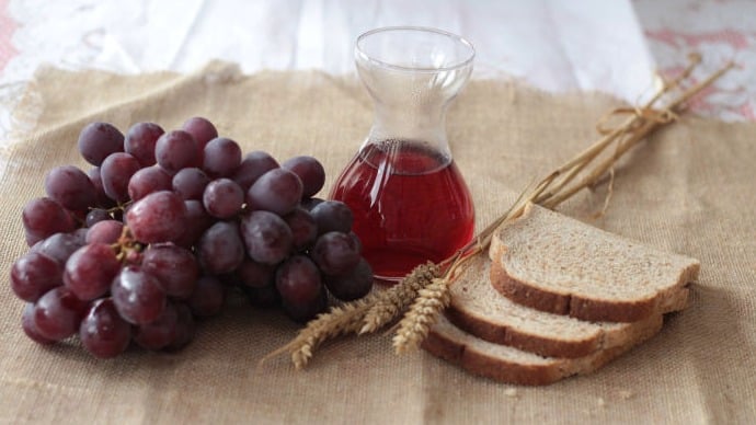 This image displays a bunch of red grapes, bread, and a small container of wine.