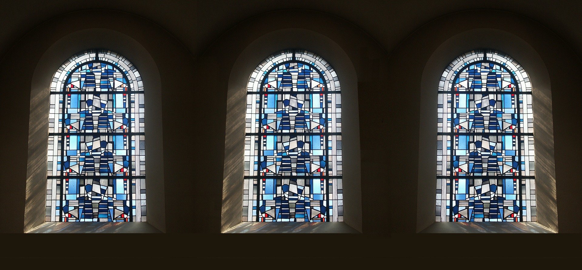 This image displays three windows with blue and white stained glass, with the sunliught shining  in.