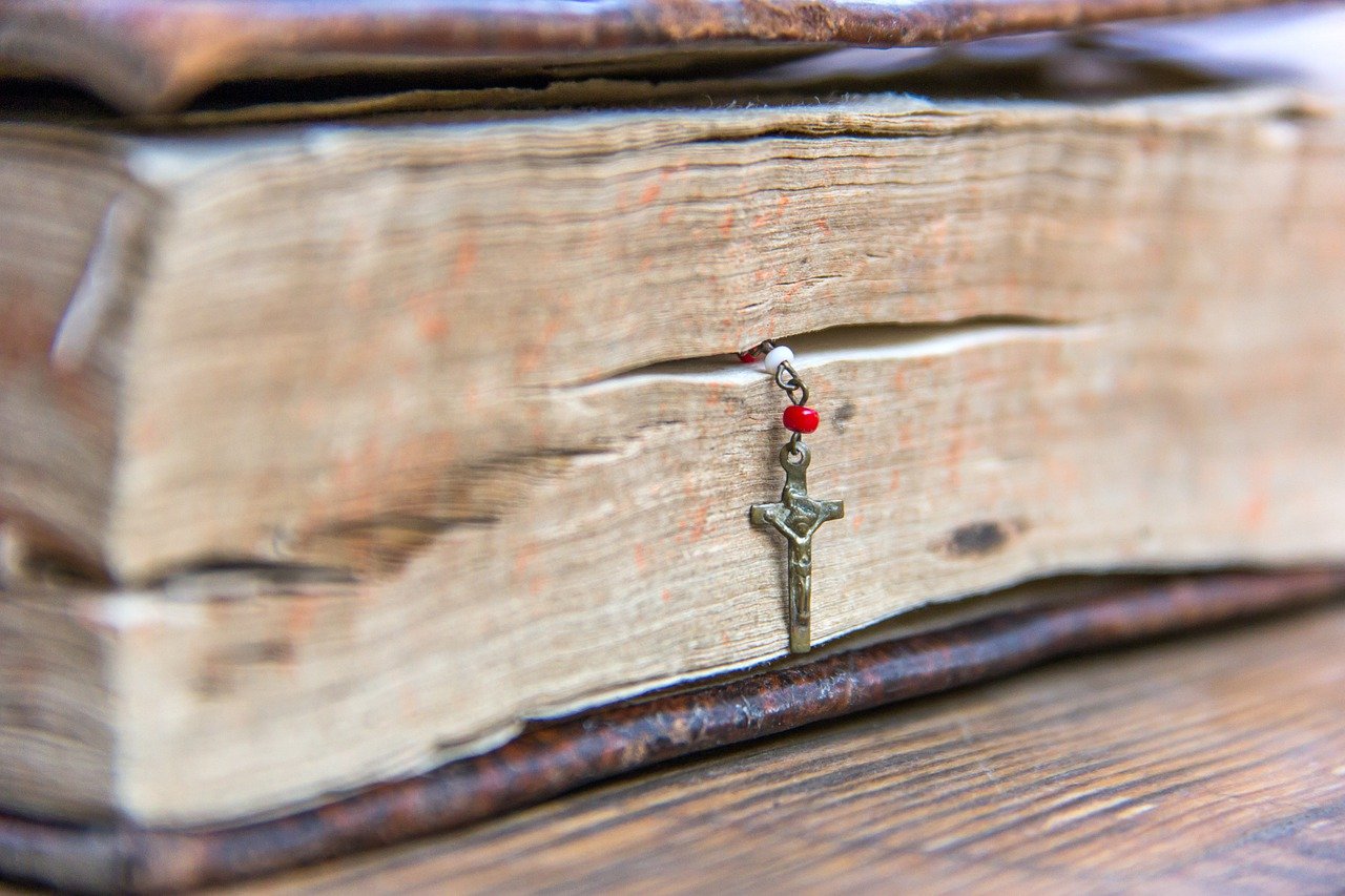This image displays an old book with a Crucifix hanging out of the pages.